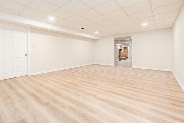 basement featuring a paneled ceiling and light hardwood / wood-style flooring