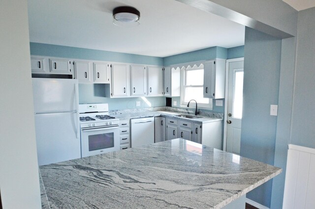 kitchen with white appliances, sink, radiator heating unit, light stone counters, and white cabinetry