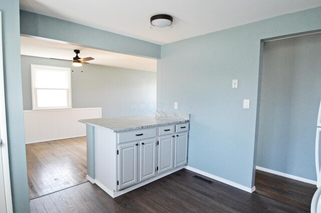 kitchen with kitchen peninsula, ceiling fan, dark wood-type flooring, and light stone counters