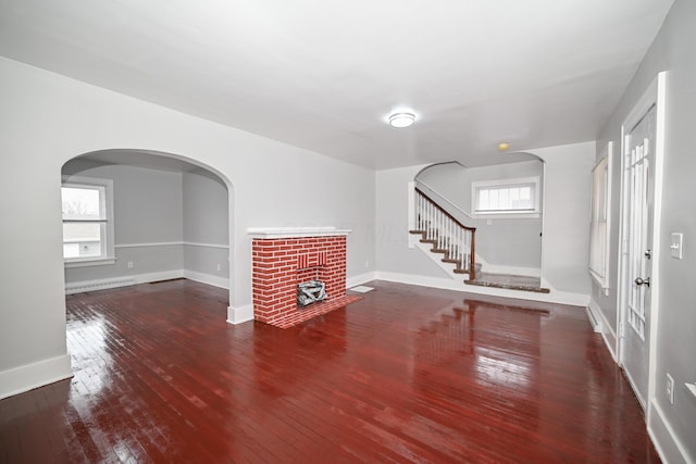 unfurnished living room with dark hardwood / wood-style flooring, baseboard heating, and a brick fireplace