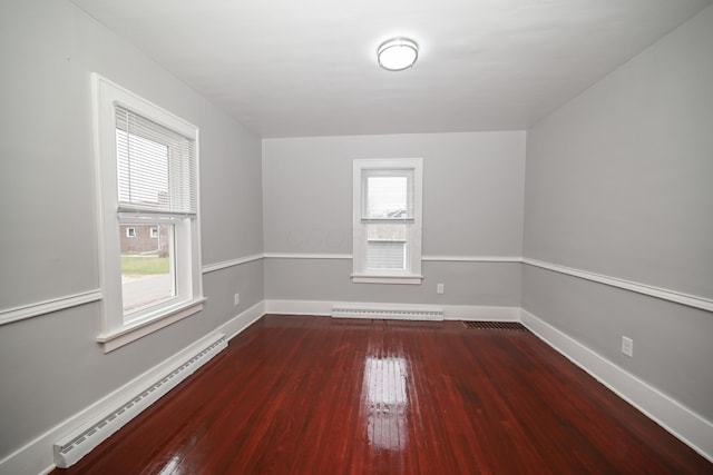 unfurnished room featuring a wealth of natural light, baseboard heating, and dark wood-type flooring