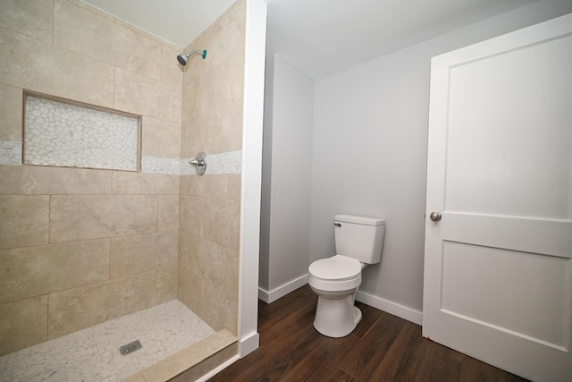 bathroom with toilet, wood-type flooring, and tiled shower