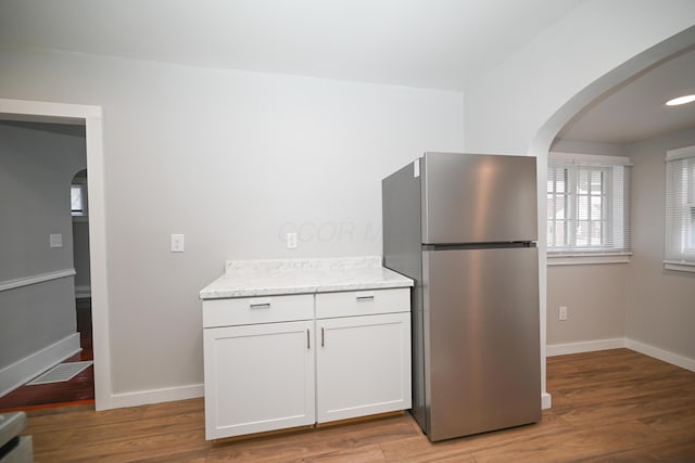 kitchen with stainless steel fridge, light stone counters, light hardwood / wood-style floors, and white cabinetry