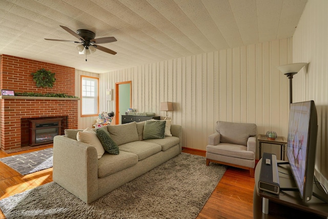 living room with ceiling fan, wood-type flooring, a textured ceiling, and a brick fireplace