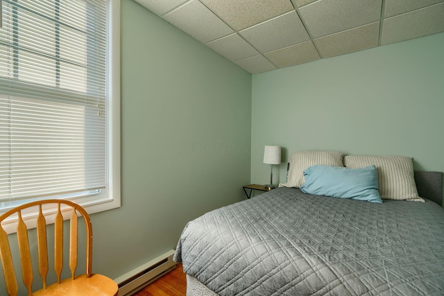 bedroom featuring hardwood / wood-style floors, a drop ceiling, and a baseboard heating unit