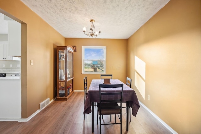 dining space featuring a chandelier, a textured ceiling, and light hardwood / wood-style flooring