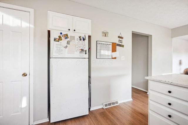 kitchen with white cabinets, white refrigerator, light stone countertops, and light hardwood / wood-style flooring