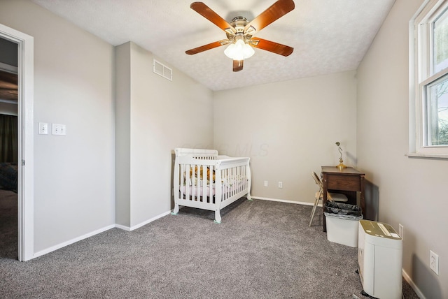 unfurnished bedroom with a crib, ceiling fan, a textured ceiling, and dark colored carpet