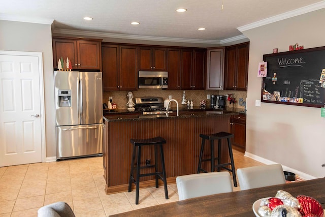 kitchen with crown molding, a kitchen island with sink, appliances with stainless steel finishes, and a breakfast bar area