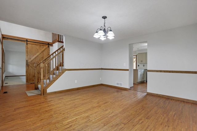 unfurnished room with a chandelier, a barn door, and light hardwood / wood-style flooring