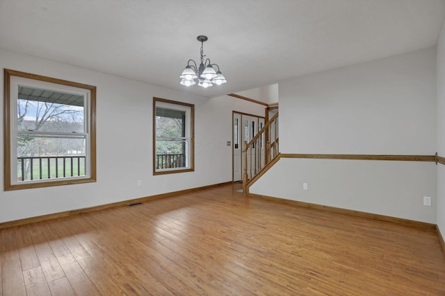 empty room featuring a chandelier, light wood-type flooring, and a wealth of natural light