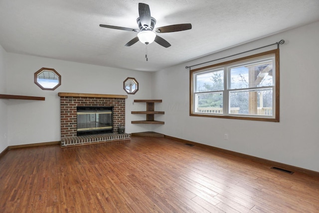 unfurnished living room featuring hardwood / wood-style flooring, ceiling fan, a fireplace, and a textured ceiling