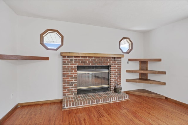 unfurnished living room featuring a healthy amount of sunlight, wood-type flooring, and a brick fireplace