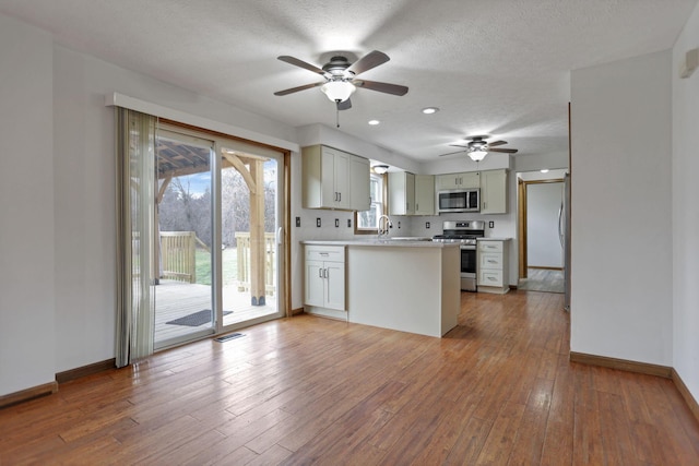 kitchen with sink, kitchen peninsula, wood-type flooring, a textured ceiling, and appliances with stainless steel finishes