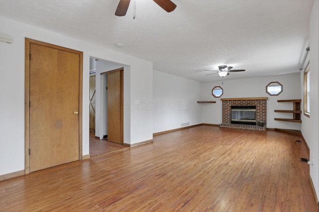 unfurnished living room featuring a fireplace, a textured ceiling, light wood-type flooring, and ceiling fan