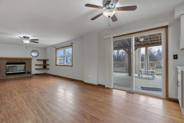 unfurnished living room with a brick fireplace, plenty of natural light, ceiling fan, and light hardwood / wood-style flooring