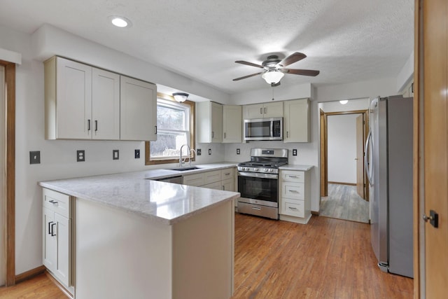 kitchen with kitchen peninsula, appliances with stainless steel finishes, a textured ceiling, sink, and light hardwood / wood-style flooring