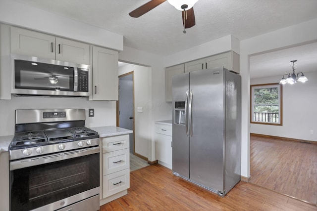 kitchen with light stone counters, light wood-type flooring, a textured ceiling, and appliances with stainless steel finishes