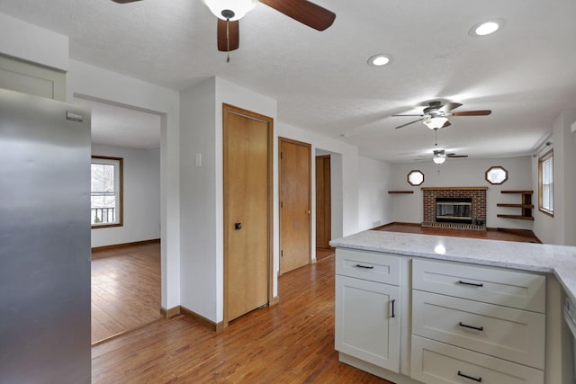 kitchen featuring white cabinets, a fireplace, a textured ceiling, light hardwood / wood-style floors, and light stone counters