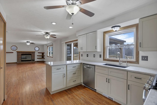 kitchen featuring a brick fireplace, stainless steel dishwasher, kitchen peninsula, white cabinets, and light wood-type flooring