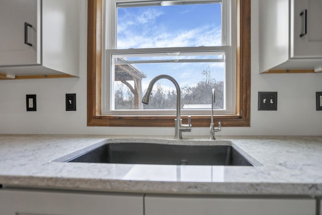 room details featuring white cabinetry, light stone countertops, and sink