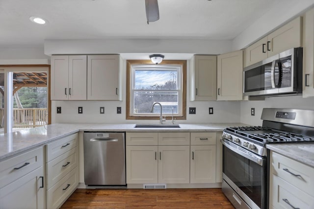 kitchen featuring light stone countertops, appliances with stainless steel finishes, ceiling fan, sink, and wood-type flooring