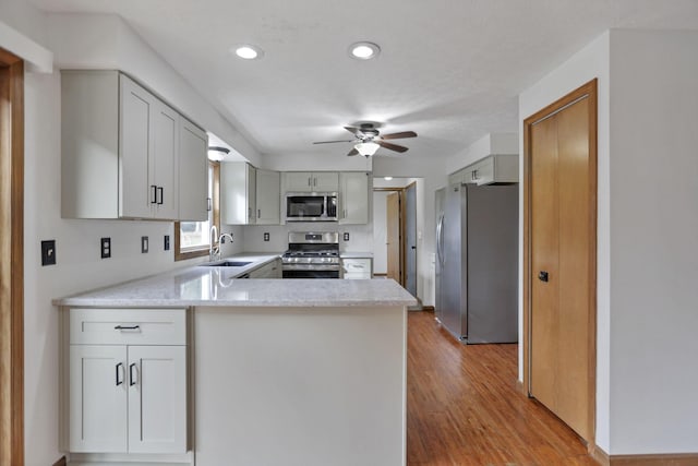 kitchen with ceiling fan, sink, light hardwood / wood-style flooring, kitchen peninsula, and appliances with stainless steel finishes