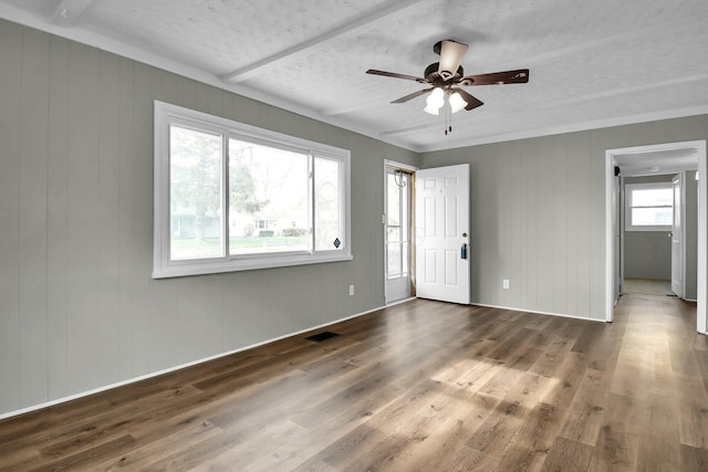 empty room with a textured ceiling, dark hardwood / wood-style floors, ceiling fan, and wooden walls