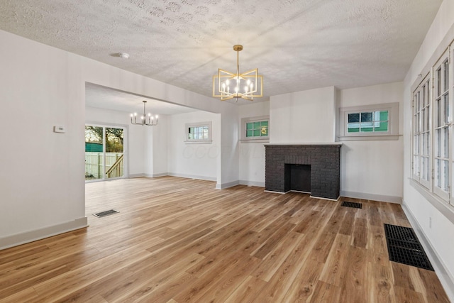 unfurnished living room featuring a fireplace, wood-type flooring, a textured ceiling, and an inviting chandelier