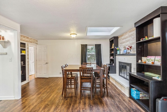 dining room with a skylight, a large fireplace, dark wood-type flooring, built in features, and a textured ceiling