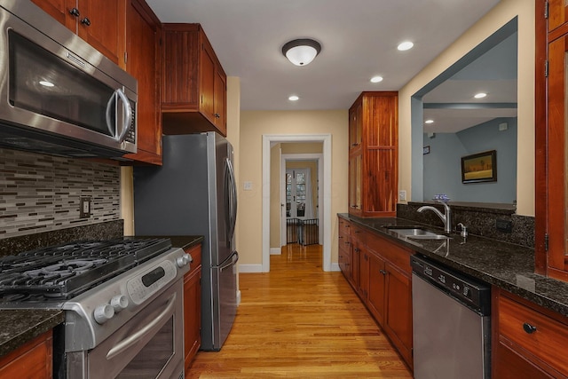 kitchen with dark stone counters, backsplash, stainless steel appliances, and light wood-type flooring