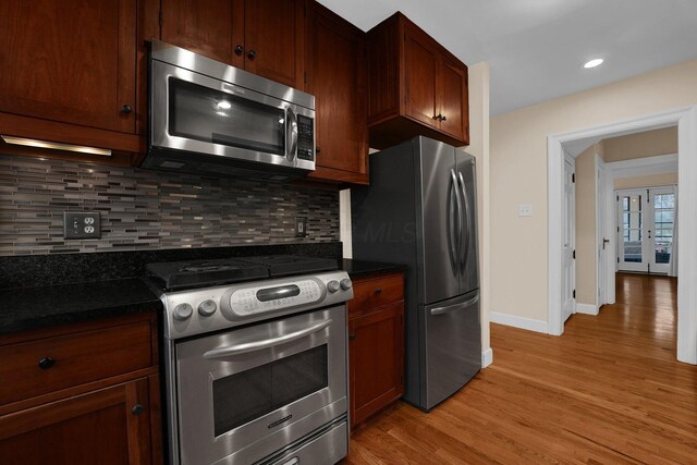 kitchen with backsplash, dark stone countertops, stainless steel appliances, and light hardwood / wood-style floors