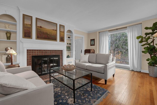 living room with ornamental molding, light hardwood / wood-style floors, built in features, and a brick fireplace