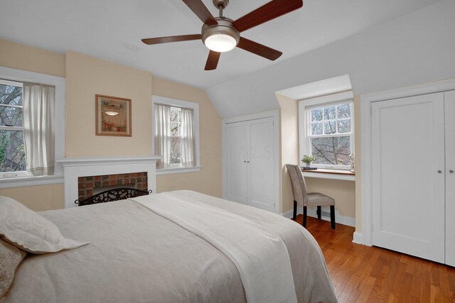 bedroom with ceiling fan, hardwood / wood-style floors, lofted ceiling, and a brick fireplace