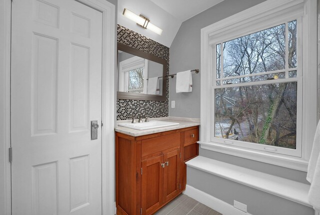 bathroom with backsplash, plenty of natural light, vanity, and vaulted ceiling