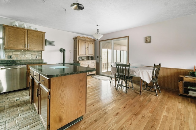 kitchen with light hardwood / wood-style flooring, dishwasher, a kitchen island, hanging light fixtures, and wood walls