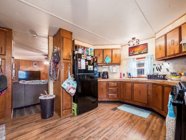 kitchen with black refrigerator, stove, wooden walls, sink, and light hardwood / wood-style flooring