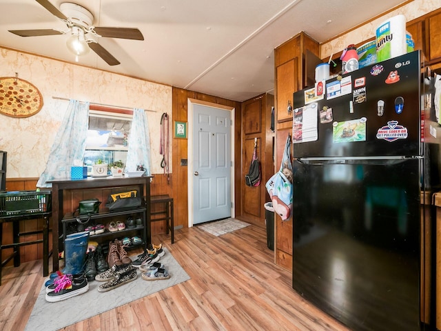 kitchen with ceiling fan, black refrigerator, light hardwood / wood-style floors, and wooden walls