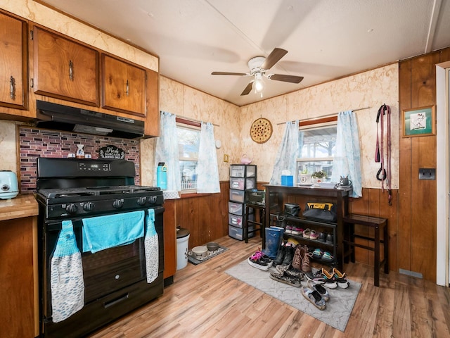 kitchen featuring ceiling fan, black gas range oven, wooden walls, and light hardwood / wood-style flooring