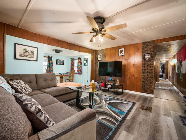 living room with hardwood / wood-style flooring, ceiling fan, and wood walls