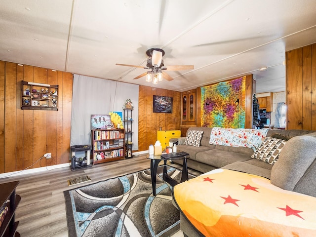 living room with hardwood / wood-style flooring, ceiling fan, and wood walls