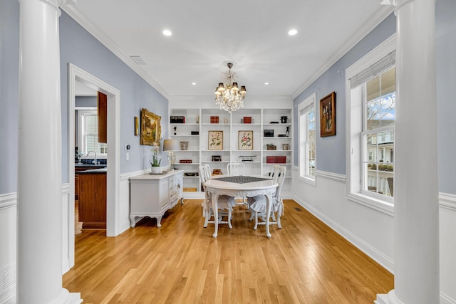 dining room with sink, ornate columns, light wood-type flooring, ornamental molding, and a notable chandelier