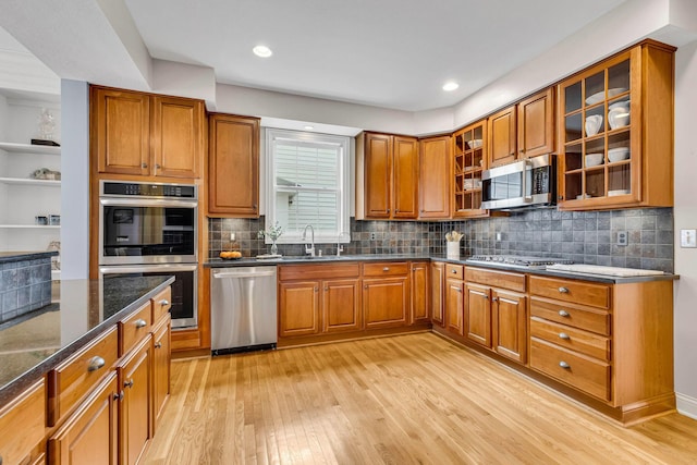 kitchen with sink, dark stone countertops, backsplash, stainless steel appliances, and light hardwood / wood-style flooring