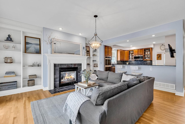 living room with built in shelves, a fireplace, and light hardwood / wood-style flooring