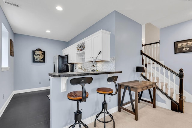 kitchen with stainless steel refrigerator, backsplash, kitchen peninsula, and white cabinets