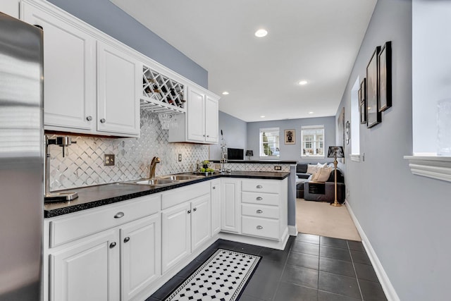 kitchen featuring sink, white cabinetry, stainless steel fridge, kitchen peninsula, and backsplash