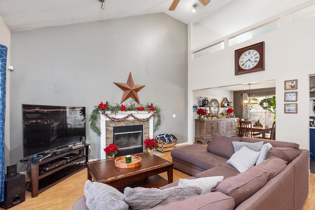 living room with a fireplace, light wood-type flooring, high vaulted ceiling, and ceiling fan