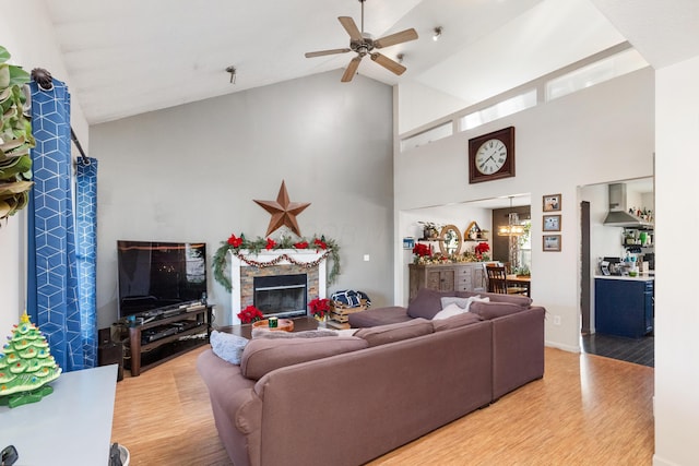 living room featuring a fireplace, wood-type flooring, high vaulted ceiling, and ceiling fan