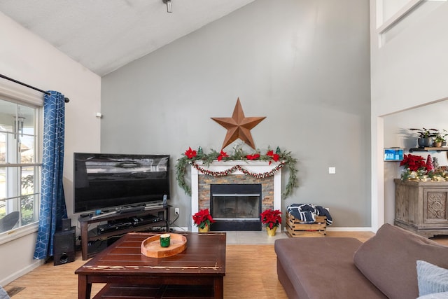 living room with light hardwood / wood-style floors, a stone fireplace, lofted ceiling, and a textured ceiling