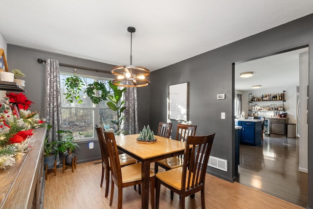 dining room featuring bar area, hardwood / wood-style floors, and an inviting chandelier